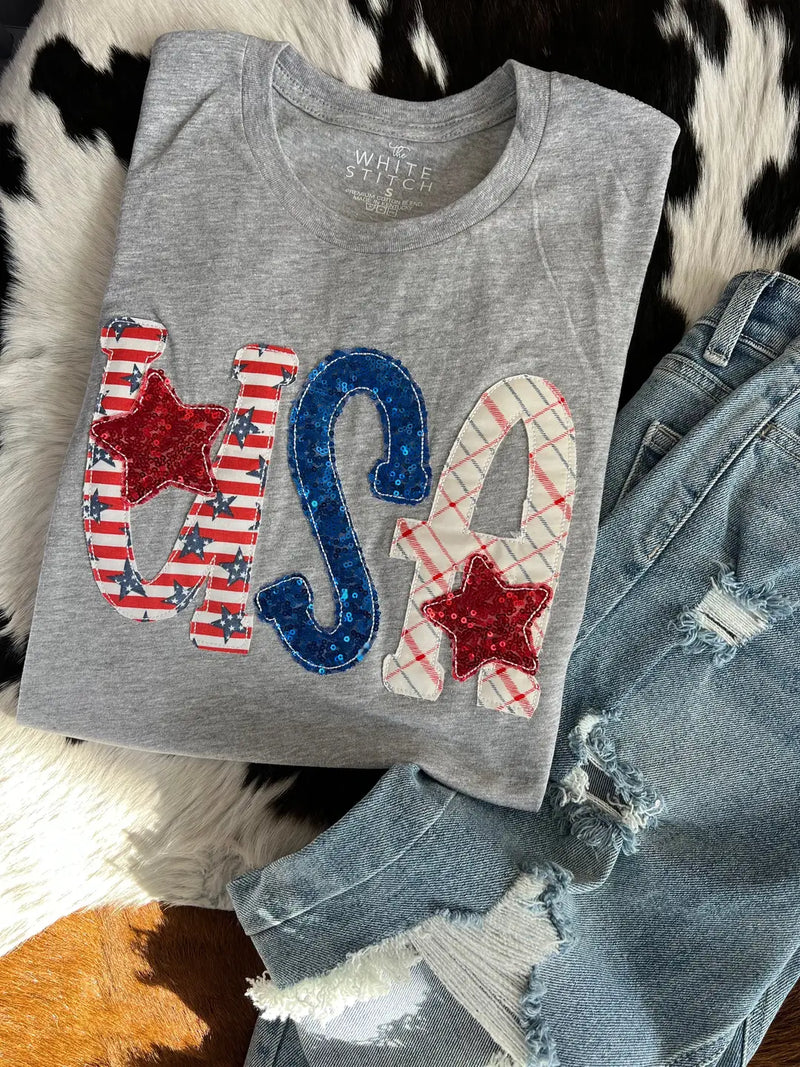 Gray tank top with 'USA' design on a textured surface with jeans.
