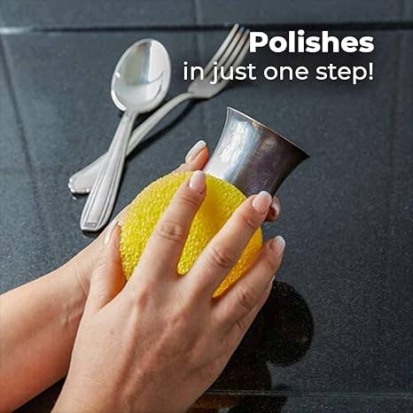 Hand using a yellow sponge to polish a silver spoon on a dark surface.