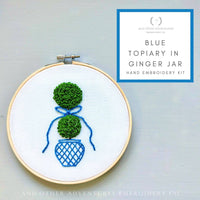 Embroidery hoop with green topiary design and blue vase on a light gray background, featuring 'And Other Adventures Embroidery Co.' branding.