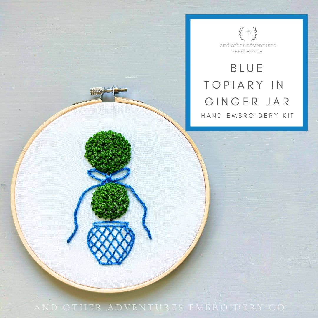 Embroidery hoop with green topiary design and blue vase on a light gray background, featuring 'And Other Adventures Embroidery Co.' branding.