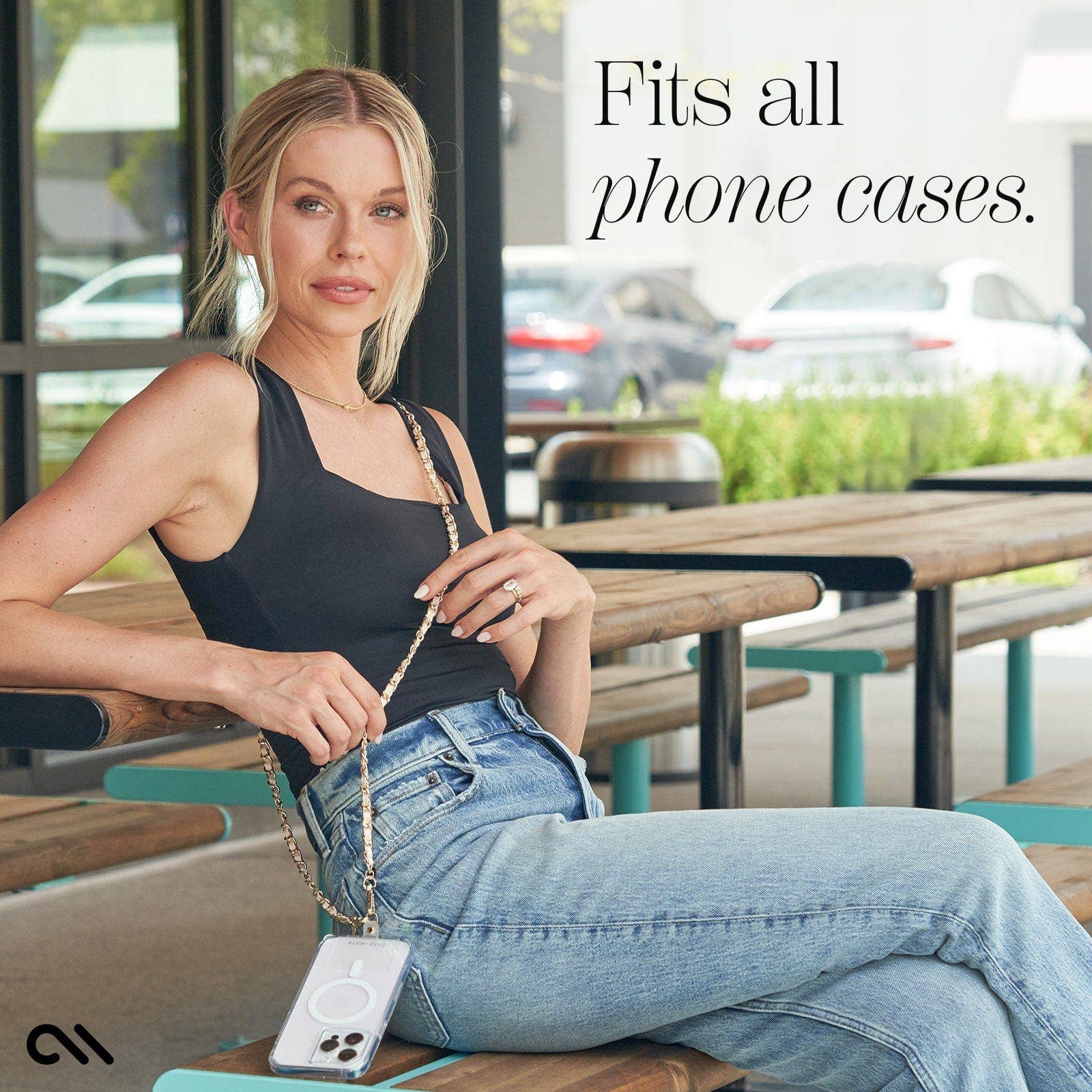 Woman sitting outdoors holding a phone case with text 'Fits all phone cases'.