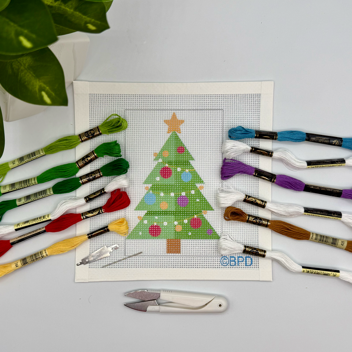 Cross-stitch kit with a Christmas tree design and embroidery floss on a light gray background.