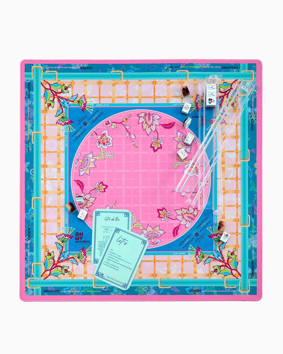 A square mahjong mat featuring a vibrant pink central circle with floral motifs, surrounded by a blue border, a white lattice grid, and a turquoise outer frame with gold accents and botanical details.