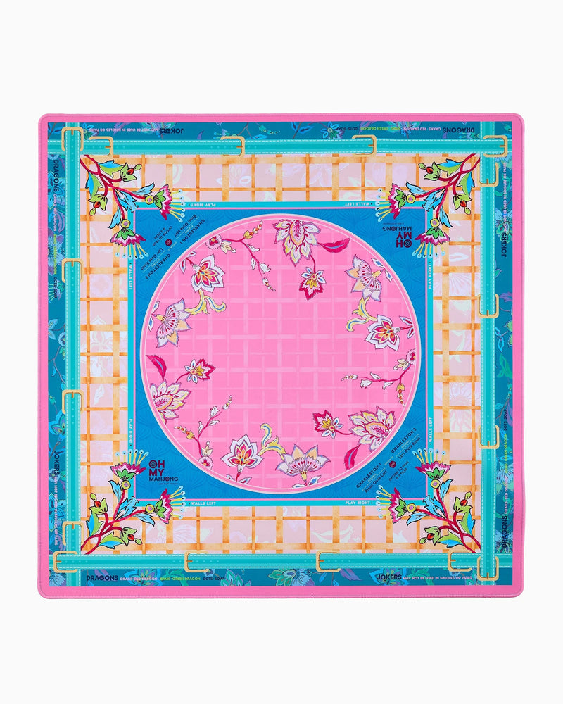 A square mahjong mat featuring a vibrant pink central circle with floral motifs, surrounded by a blue border, a white lattice grid, and a turquoise outer frame with gold accents and botanical details.