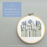 Embroidery kit with floral design in a hoop on a gray background, featuring the brand 'And Other Adventures Embroidery Co'.