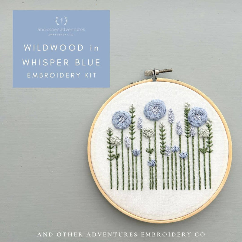 Embroidery kit with floral design in a hoop on a gray background, featuring the brand 'And Other Adventures Embroidery Co'.