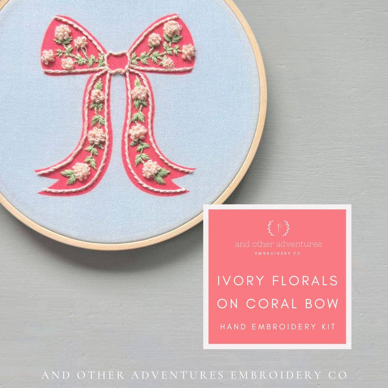 Embroidery hoop with pink floral bow design on a gray background, featuring 'And Other Adventures Embroidery Co' branding.