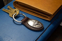 Keychain with emblem on a blue surface next to a brown leather wallet