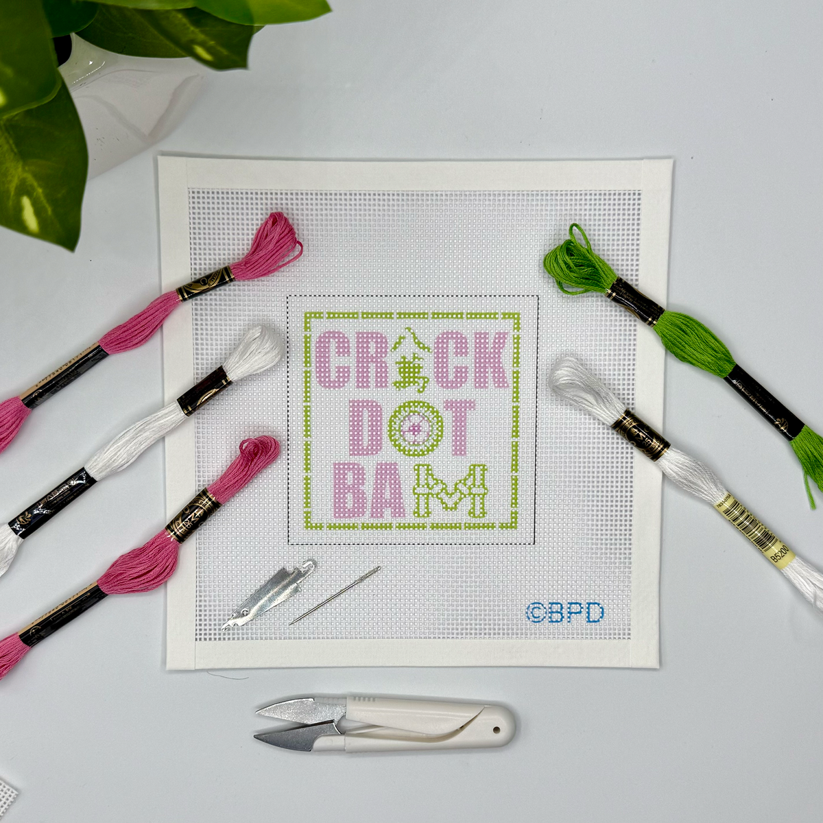 Cross-stitching kit with 'CRICK DOT BAM' design on a white fabric background, surrounded by embroidery threads and tools.