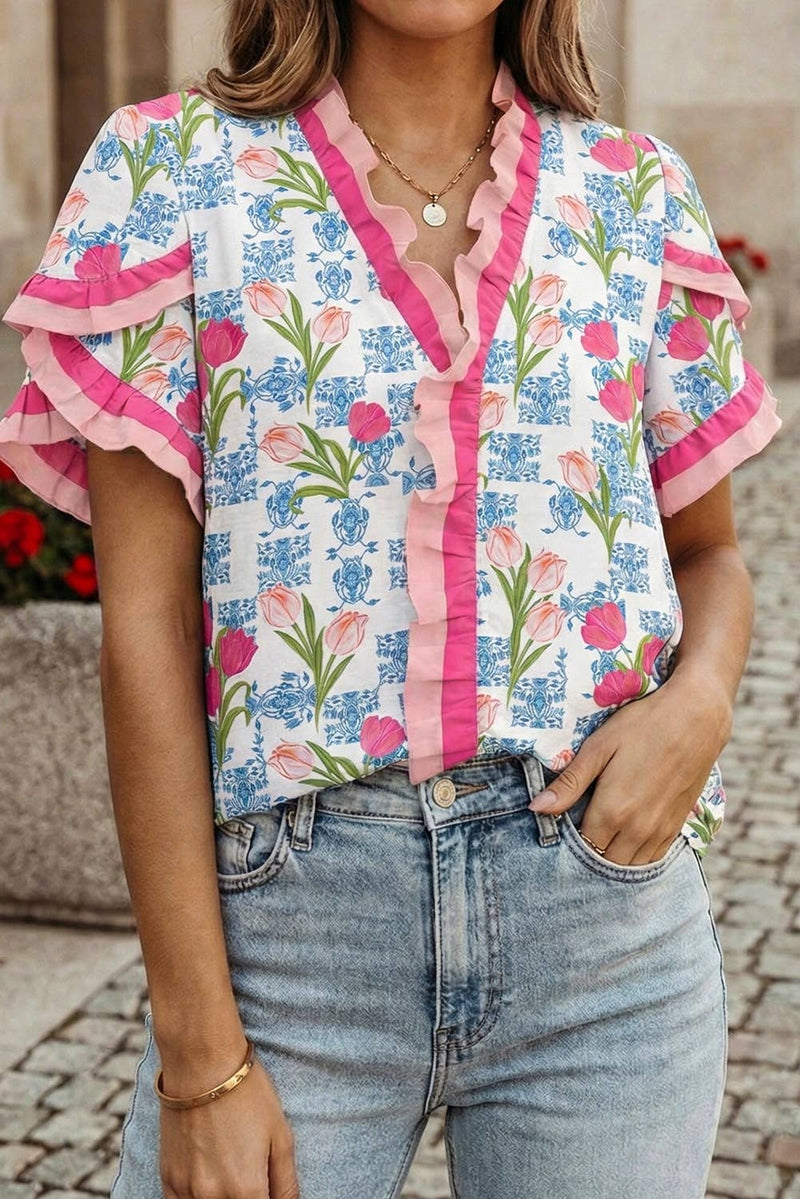 Woman wearing a floral blouse with pink accents and jeans, standing outdoors.