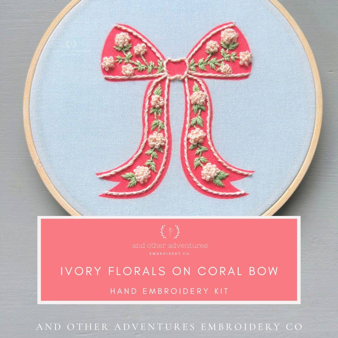 Embroidery hoop with pink bow design on light blue fabric, brand 'And Other Adventures Embroidery Co' visible.