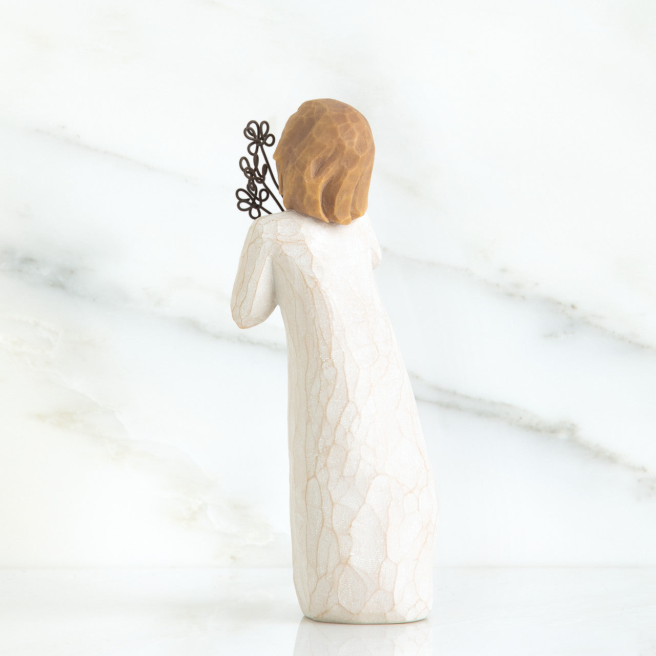 White ceramic figurine with textured surface and brown hair accessory on a marble background