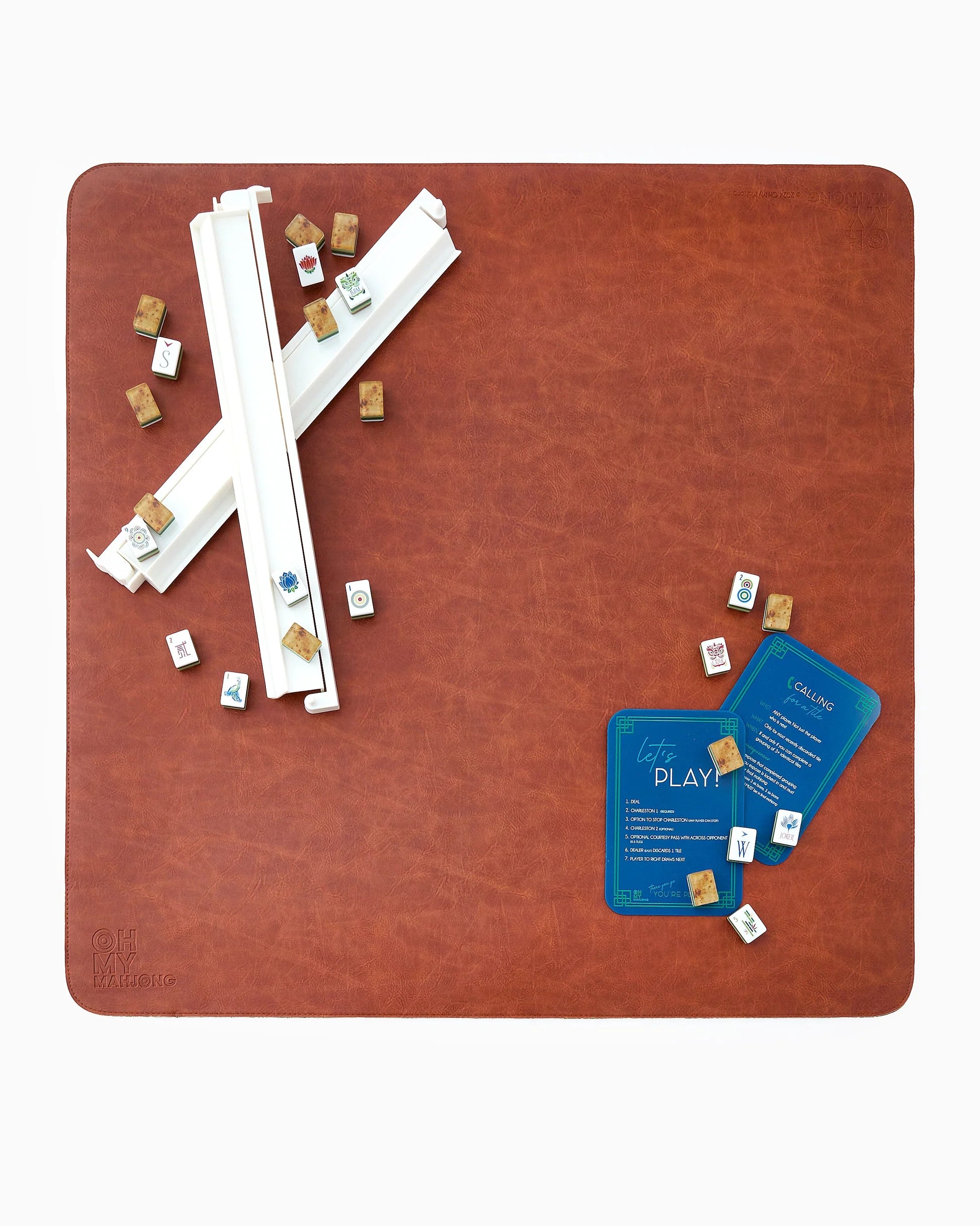 Brown leather Mahjong Mat with tiles, racks. pushers, and game cards on table on a white background