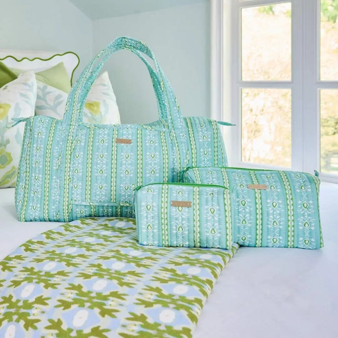 A matching fabric diaper bag set with a vertical striped pattern in mint green, aqua, and white, displayed on a bed next to a matching patterned blanket. The set includes a large tote bag, a medium pouch, and a small zippered pouch.