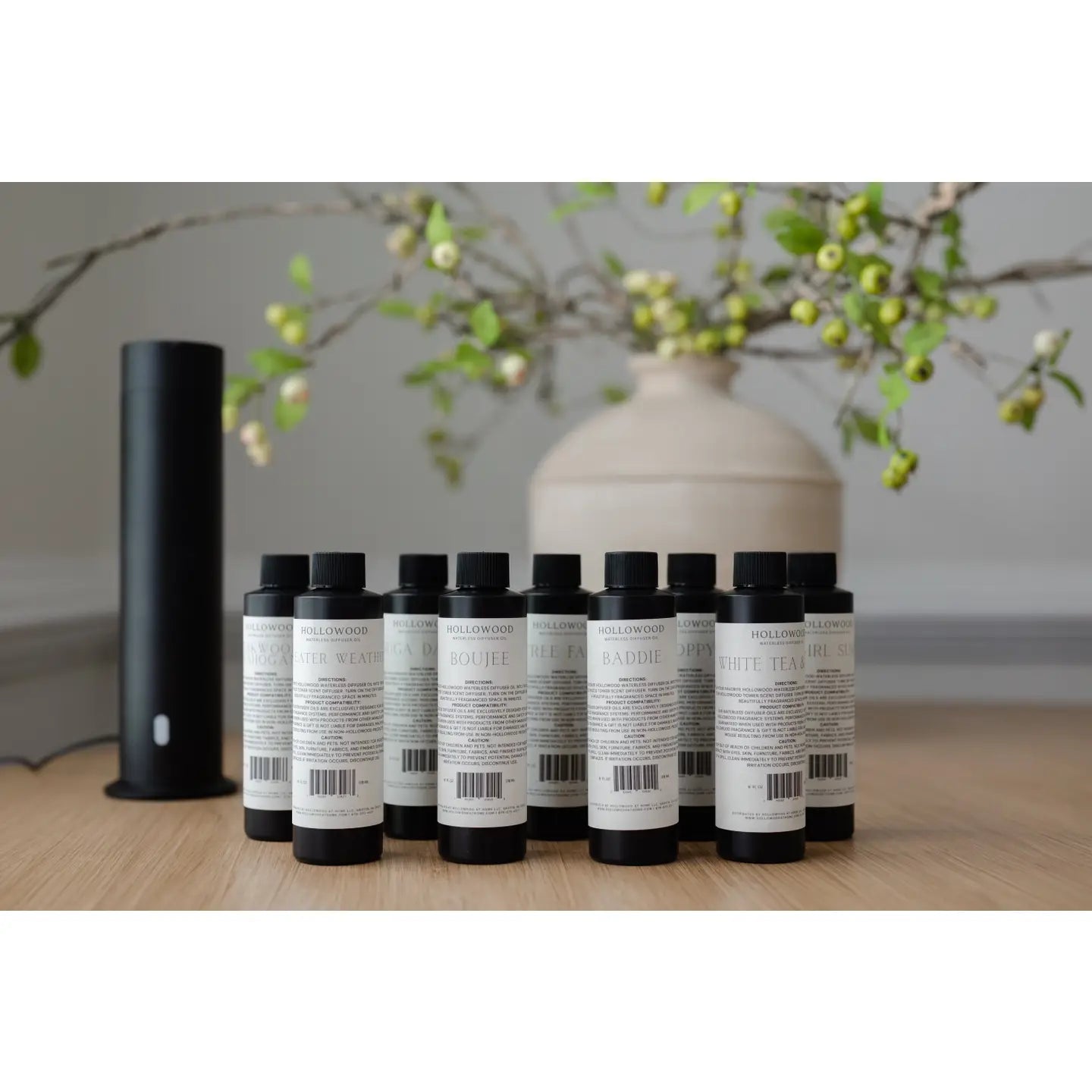 Row of black and white bottles on a wooden surface with a decorative vase and branches in the background.