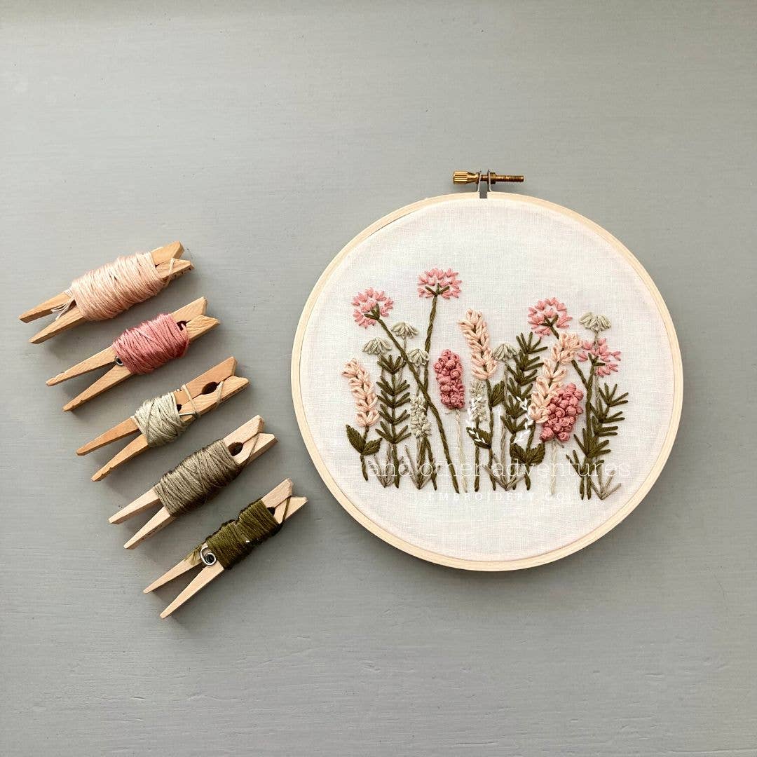 Embroidery hoop with floral design and wooden clothespins with thread on a gray background