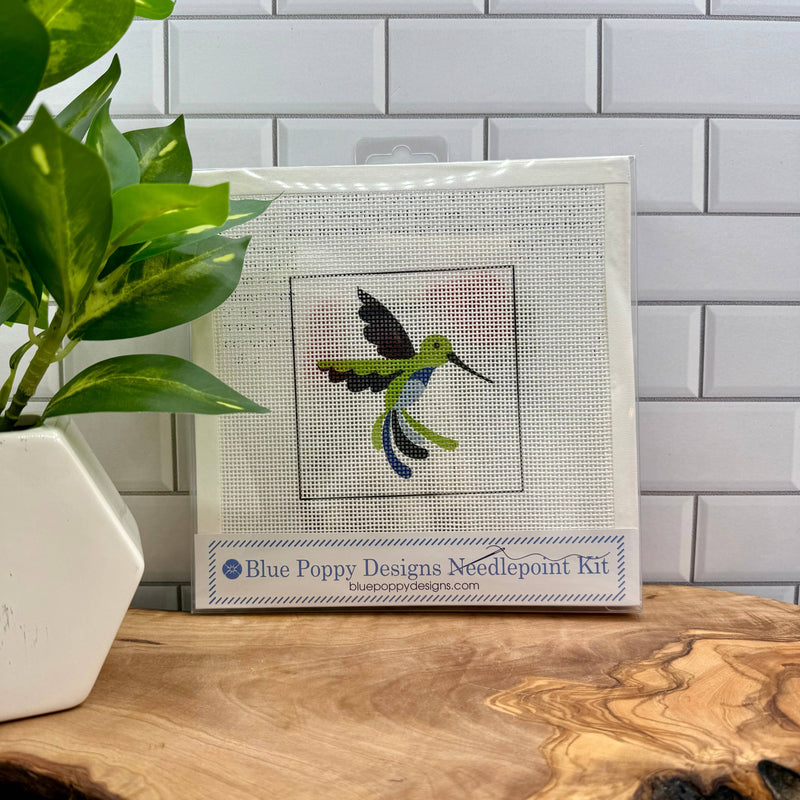 Blue Poppy Designs needlepoint kit with a hummingbird design on a wooden surface.