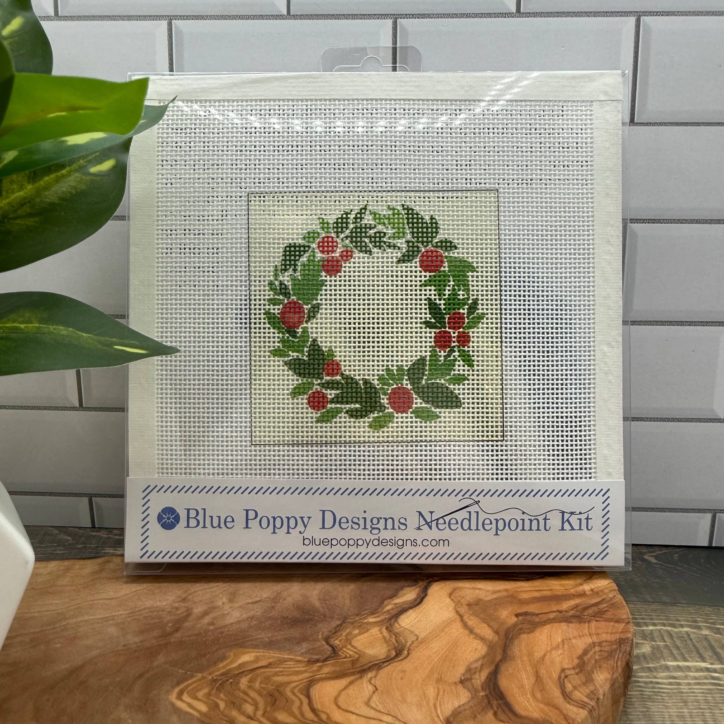 Blue Poppy Designs needlepoint kit with a wreath design on a wooden surface.