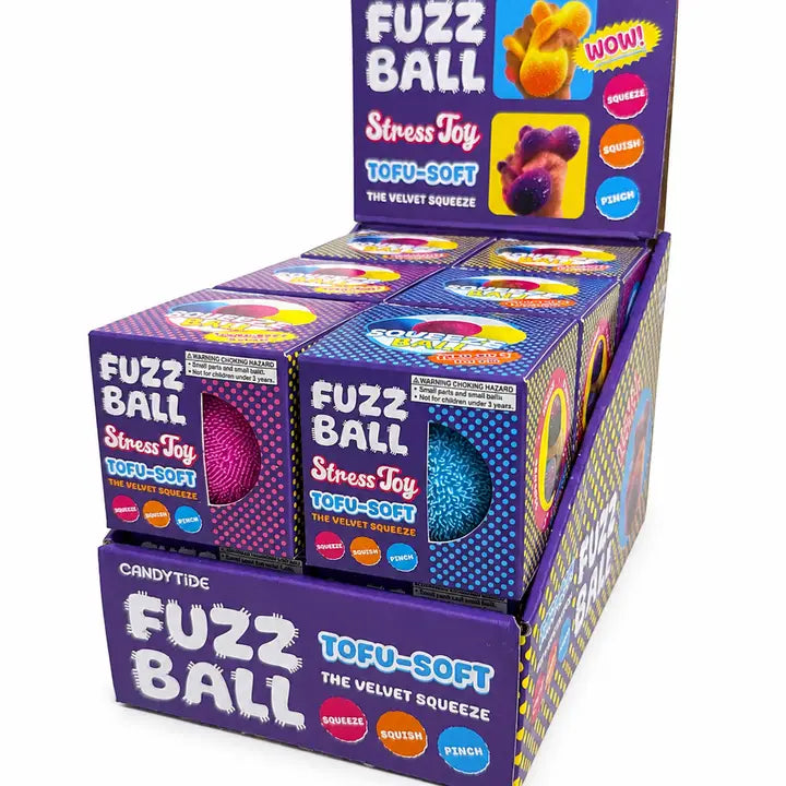 A retail display box filled with multiple individual boxes of Fuzz Ball Stress Toys. The packaging is predominantly purple with white text and colorful graphics showing the different colored fuzz balls inside.