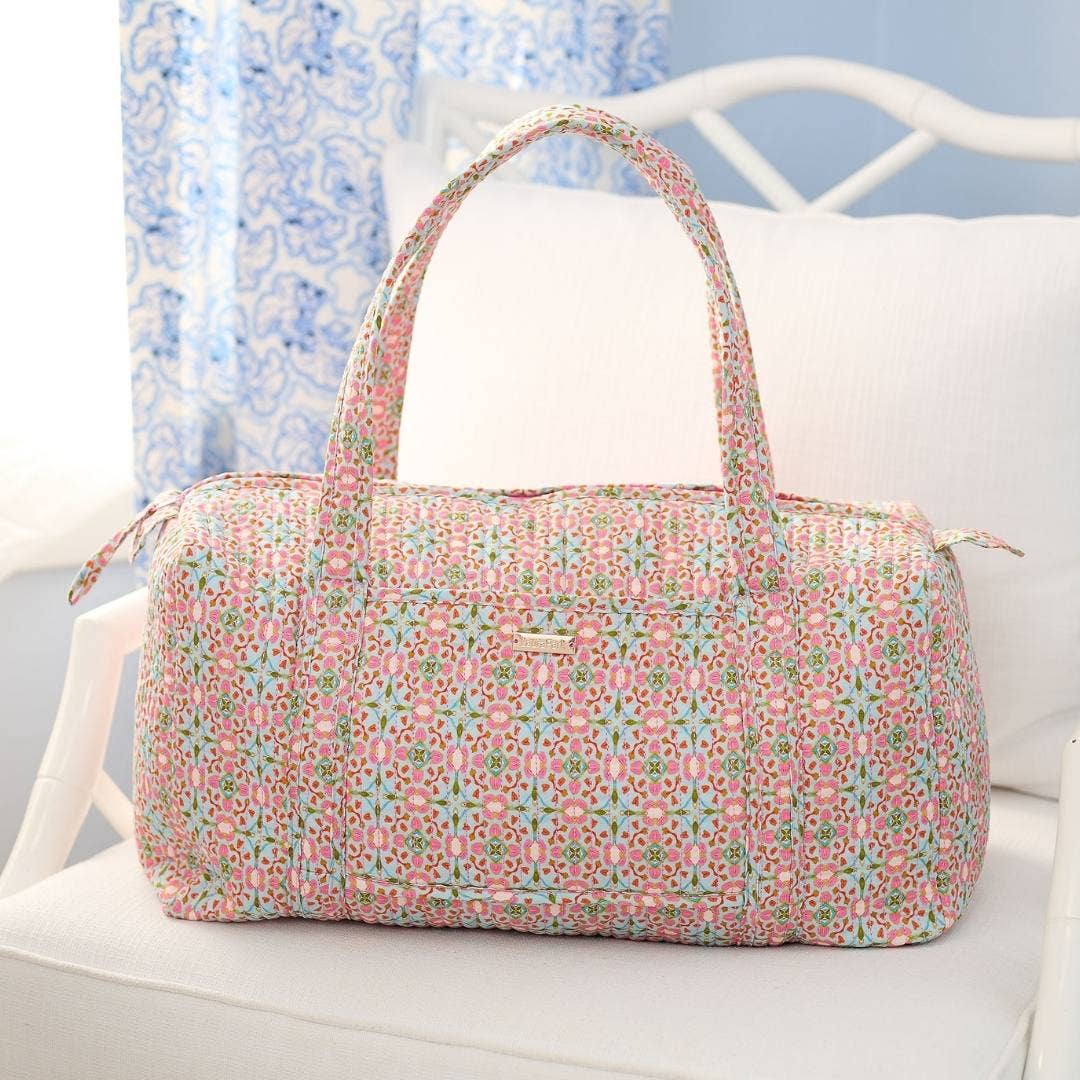 Floral patterned duffel bag on a white surface with a light blue floral curtain in the background