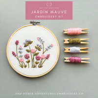 Embroidery kit with floral design, threads, and branding on a gray background