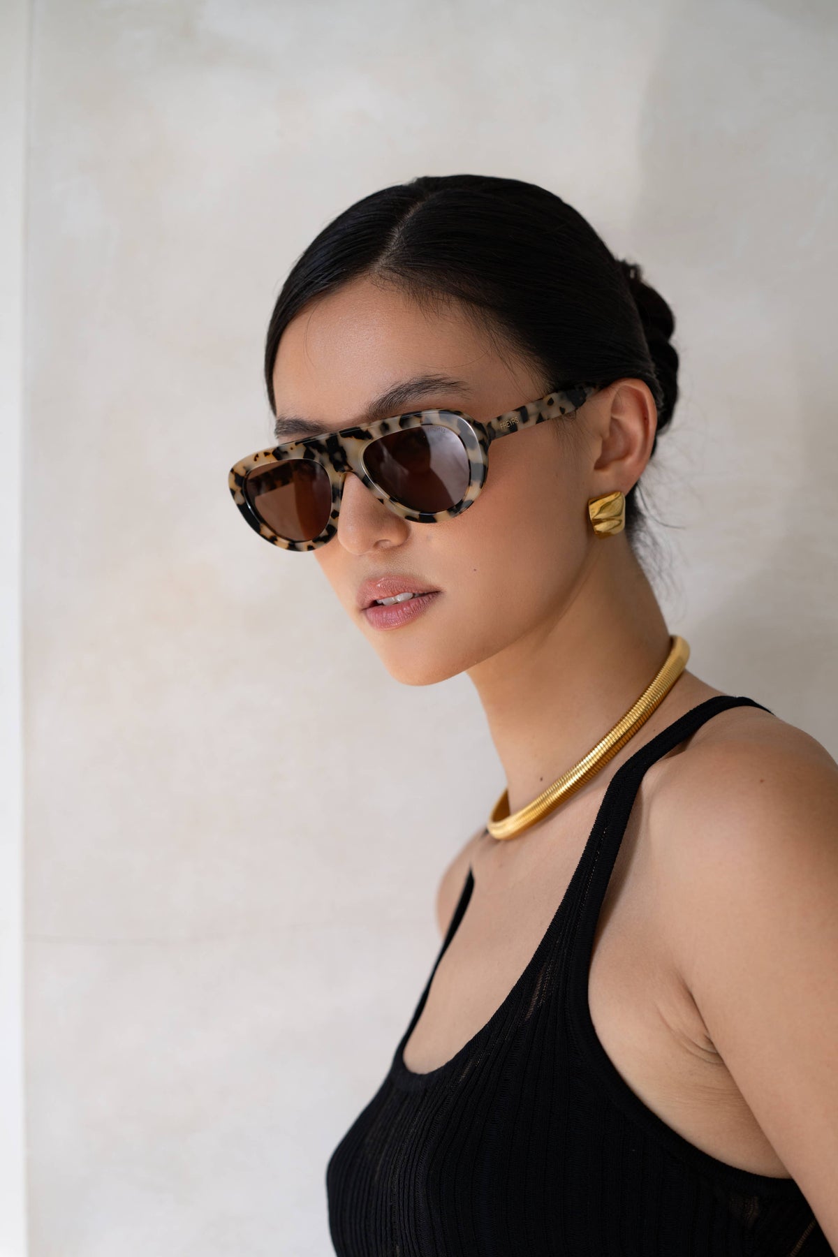Woman wearing leopard print sunglasses and a black top against a white background