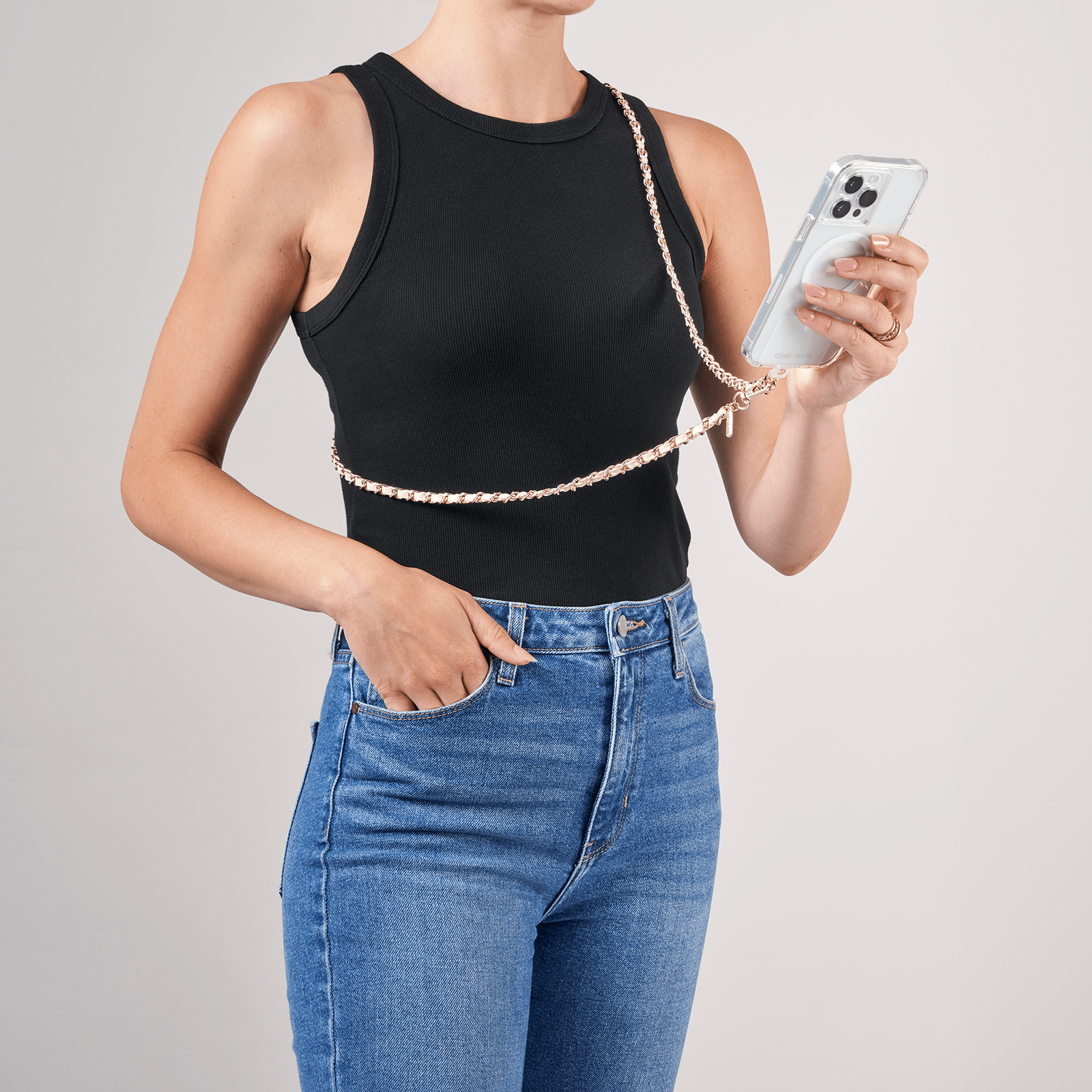 Person wearing a black sleeveless top and blue jeans, holding a phone with a chain strap.