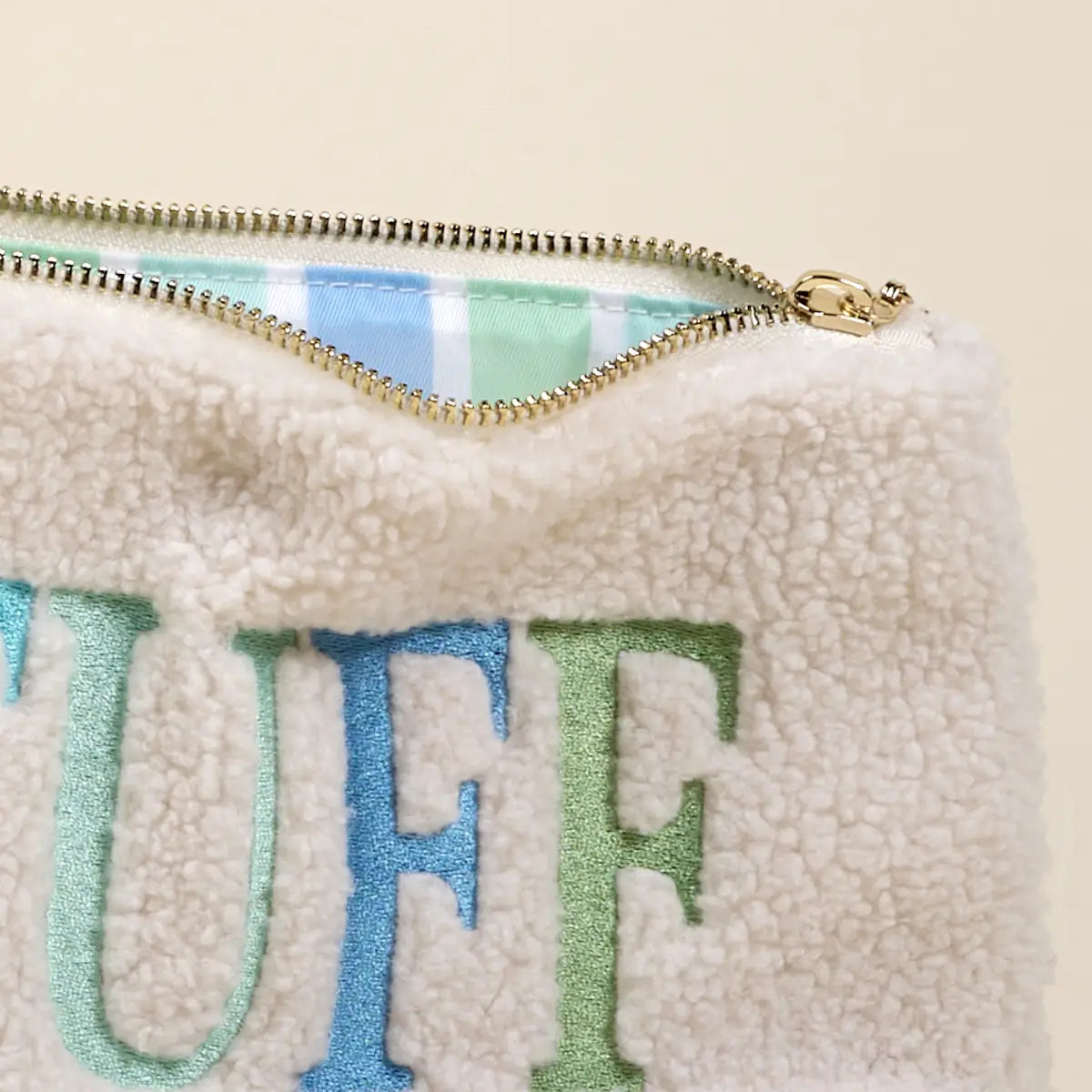 White sherpa pouch with 'UFF' text in blue and green on a beige background
