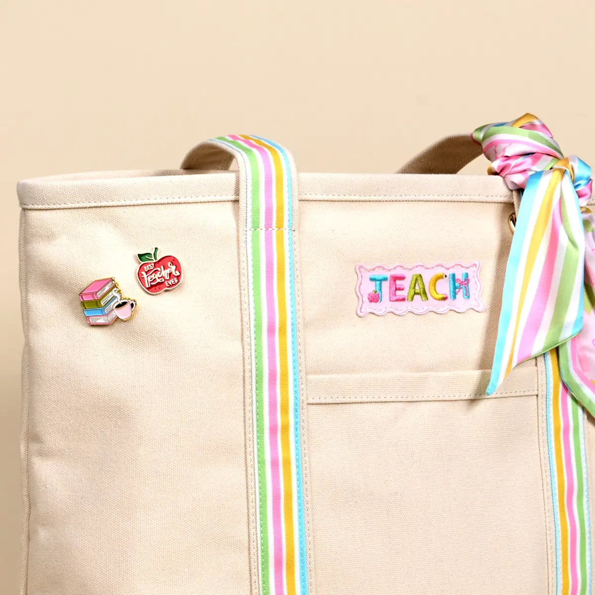 Beige tote bag with colorful ribbons and educational-themed pins on a beige background