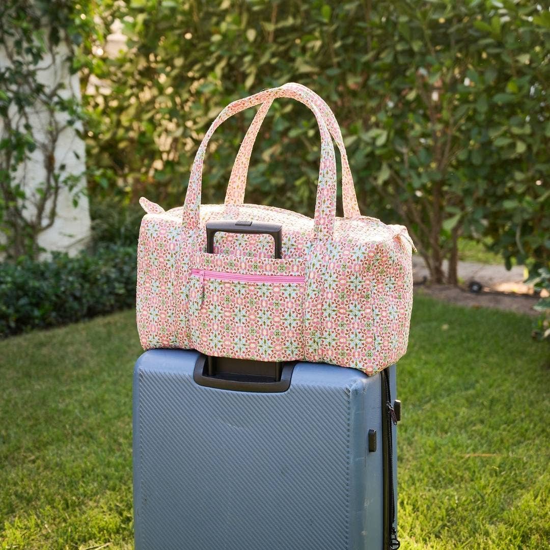 Floral patterned duffel bag on top of a blue suitcase outdoors.