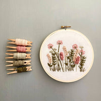 Embroidery hoop with floral design and thread spools on a gray wall