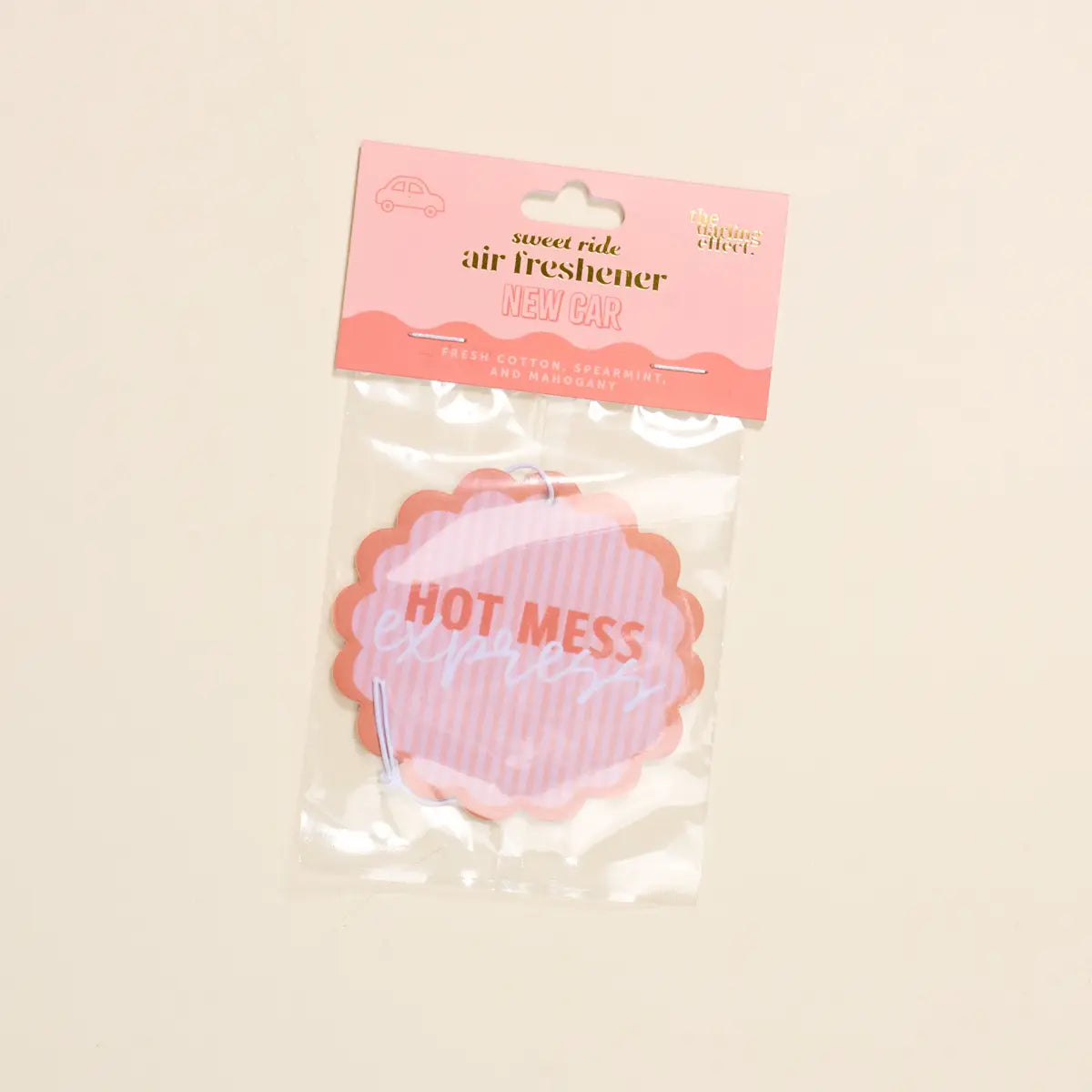 Pink air freshener labeled 'Hot Mess' in clear packaging on a beige background