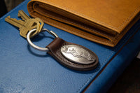 Brown leather keychain with metal emblem on a blue surface