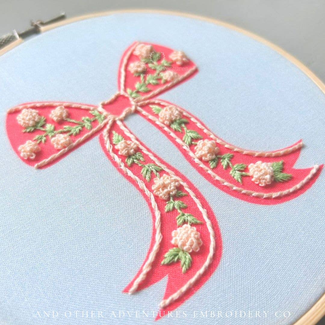 Embroidery of a pink bow with floral details on light blue fabric.