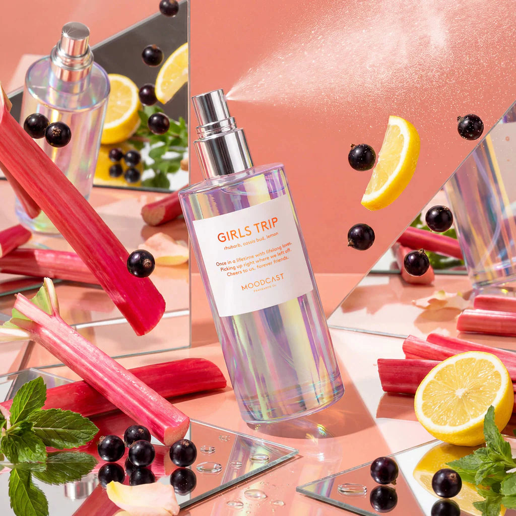 Bottle labeled 'Girls Trip' surrounded by lemons, rhubarb, and blackberries on a reflective surface.