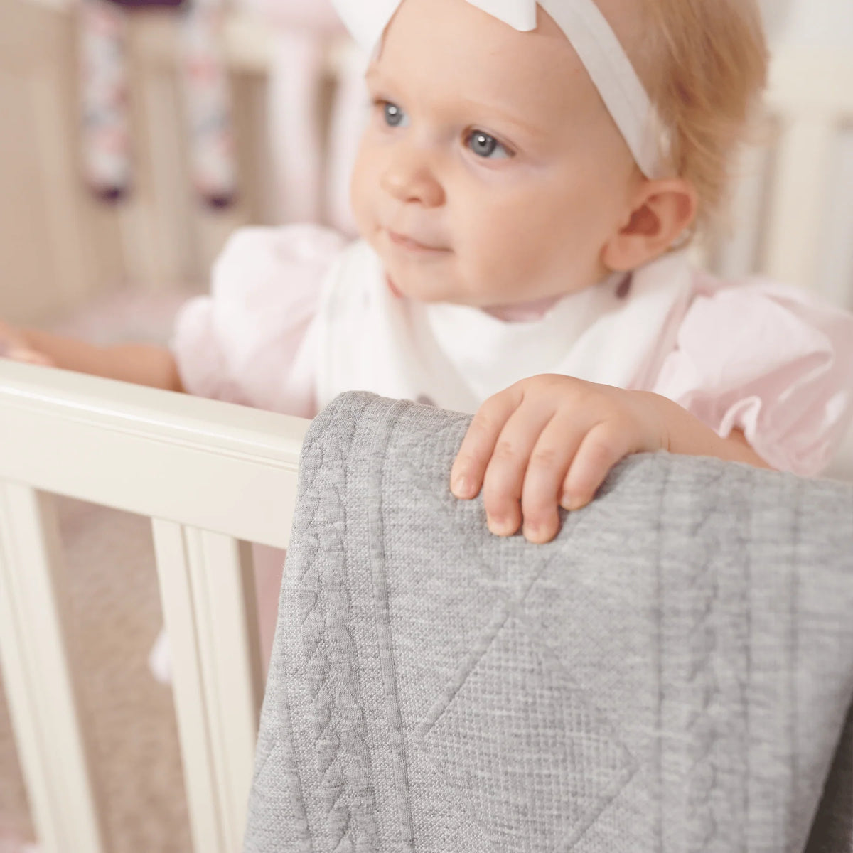 Baby in a crib with a gray blanket
