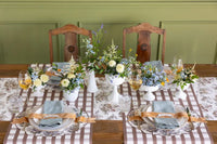 Dining table set with floral centerpieces, glasses, and cutlery against a green wall.