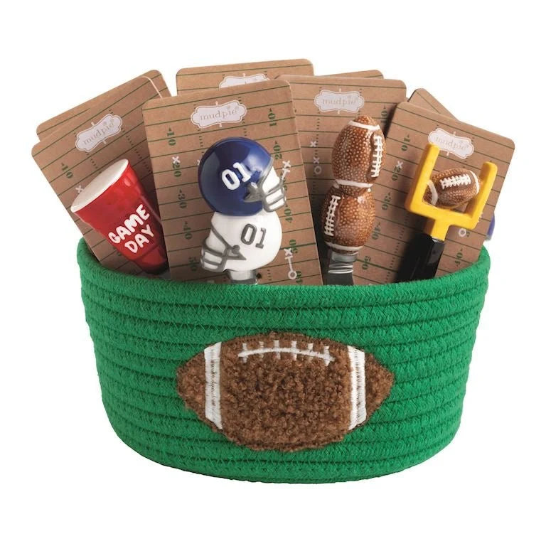 Green woven basket with football-themed items including a cup, helmet, and cards on a white background