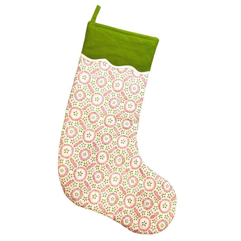 A Christmas stocking with a green velvet cuff and hanging loop, featuring a pink and green circular medallion pattern on a white background.