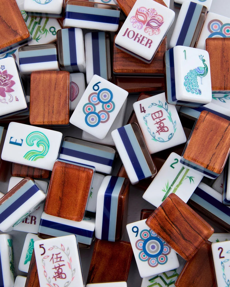 A pile of Mahjong tiles showing both the white backings with blue stripes and the wooden tops, including a visible 'JOKER' tile and numbered tiles with traditional Chinese and Western motifs.