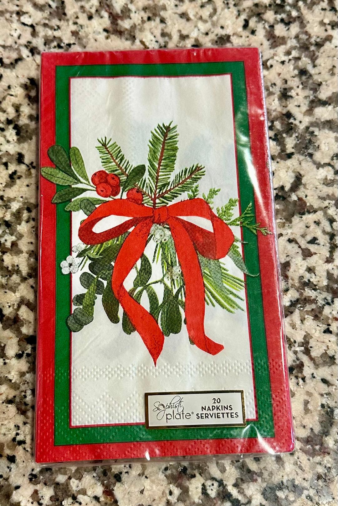 Packaged holiday-themed napkins with red ribbon and greenery on a granite surface