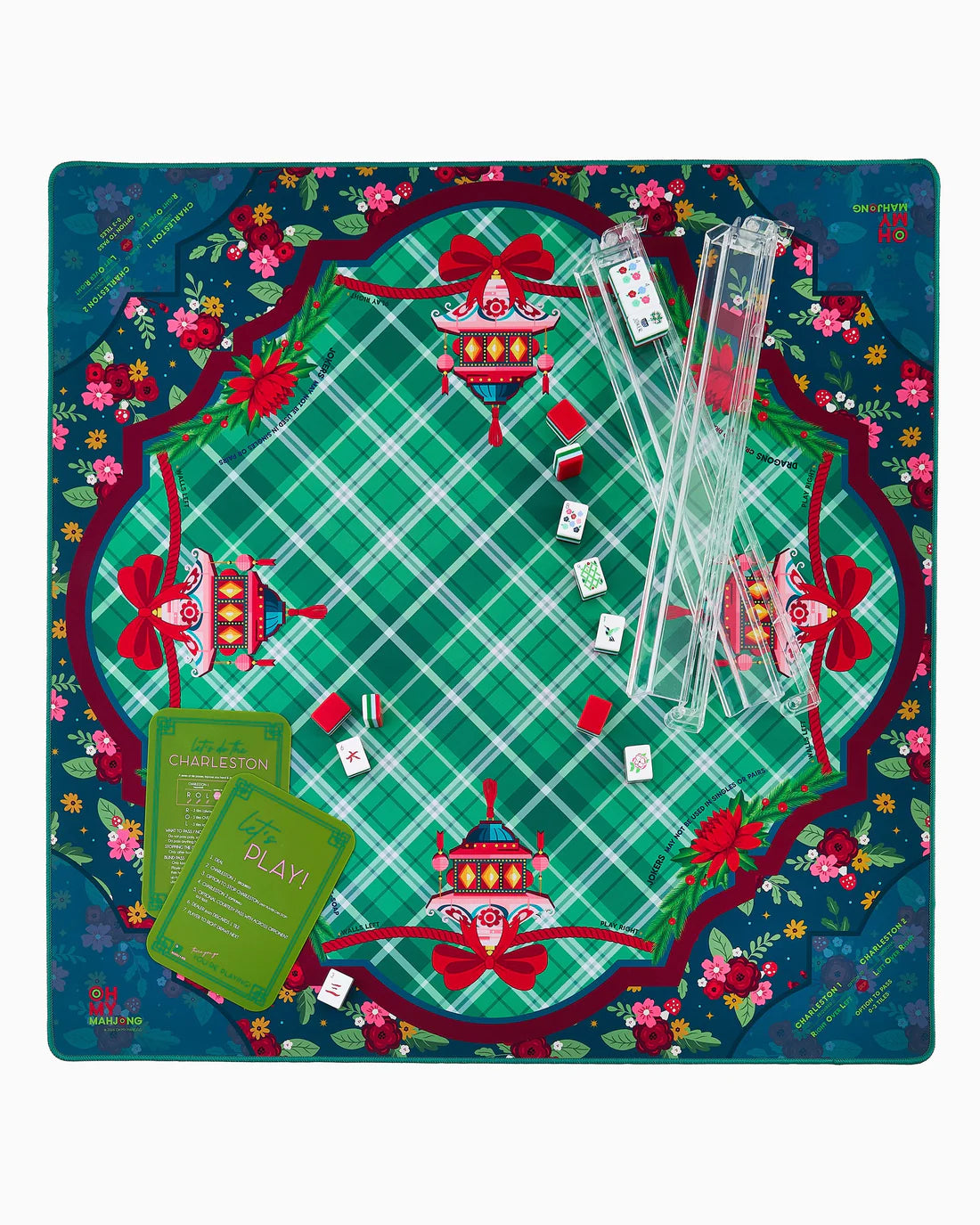 A mahjong mat laid out flat on a white background, featuring a green plaid game board with red decorative borders, floral accents, playing cards, clear dice, and green instruction cards.