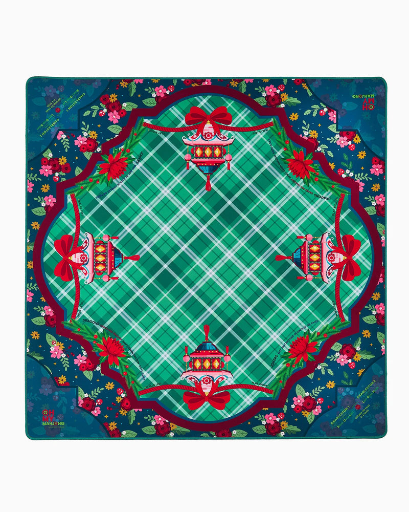 A mahjong mat featuring a festive Christmas-themed pattern with a green and white plaid center, red bows, ornaments, and a floral border on a dark teal background.